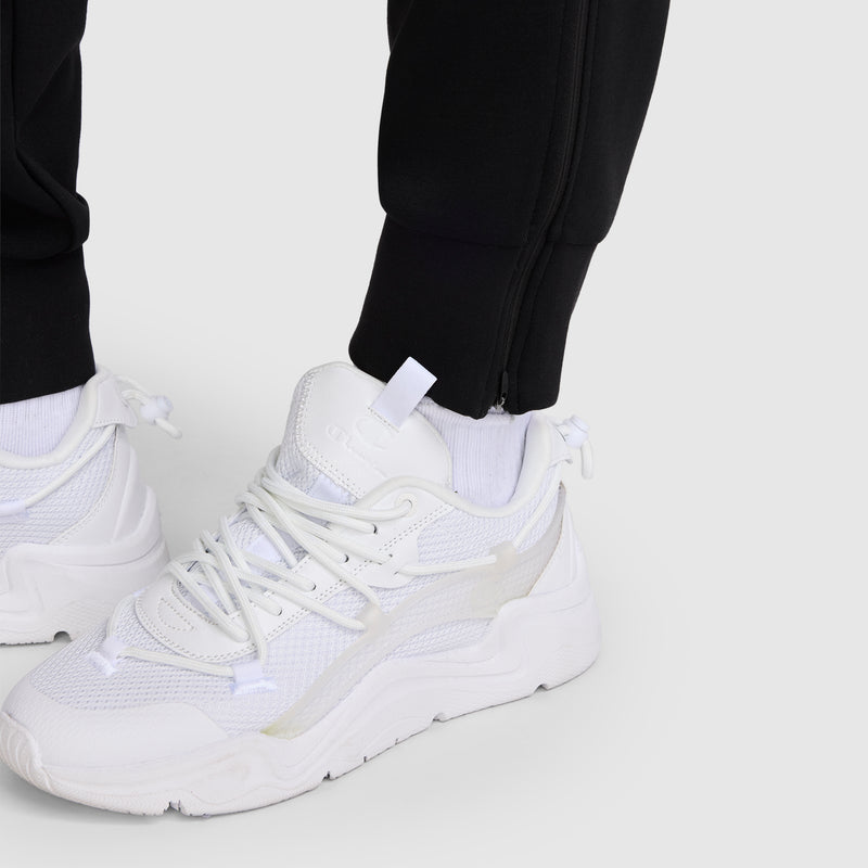A person wearing white sneakers and the Champion Taper Leg Jogger with Zippers stands on a light gray surface.