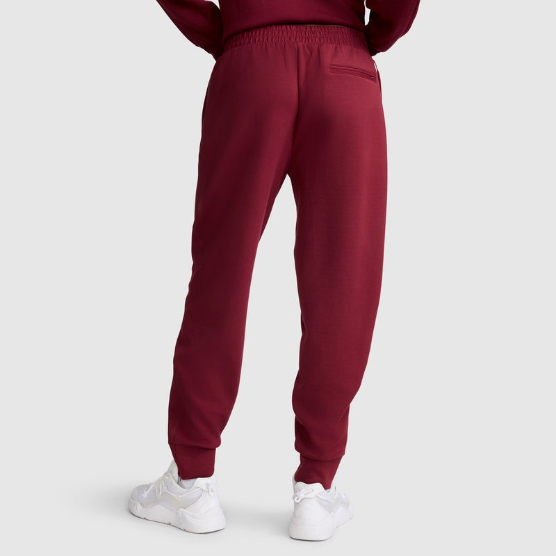 A person is shown from the back, standing against a plain light gray background, wearing Champion's maroon Taper Leg Jogger with Zippers paired with a matching sweatshirt and white sneakers.