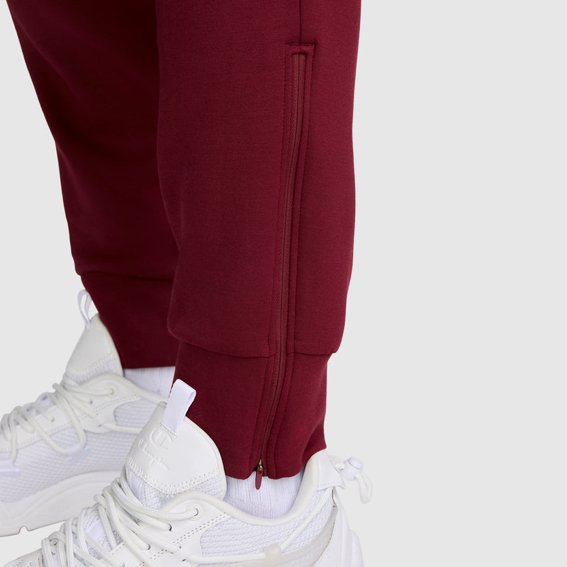 Close-up of a person wearing Champion Taper Leg Jogger with Zippers in maroon and white athletic shoes, set against a plain light gray background.