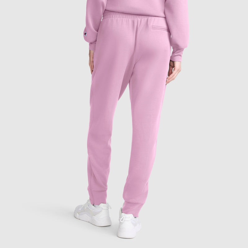 A person wearing Champion Taper Leg Jogger with Zippers in light pink, paired with a matching pink sweatshirt and white sneakers, stands with their back to the camera against a plain white background.