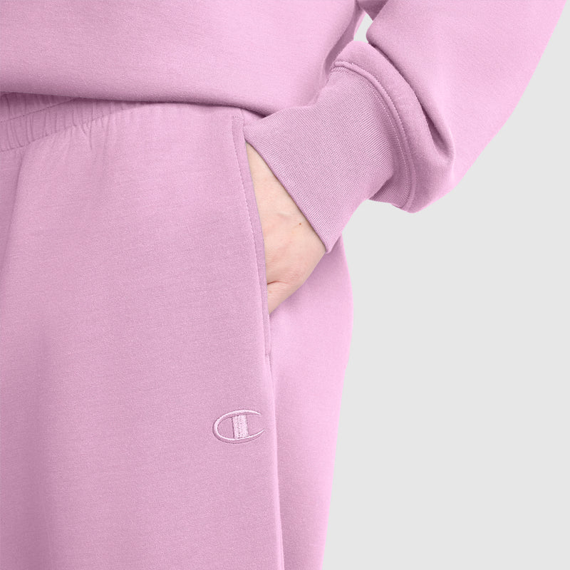 A person is wearing a light purple sweatshirt and the Champion Taper Leg Jogger with Zippers, with a hand in their pocket. The Champion logo is visible on the jogger.