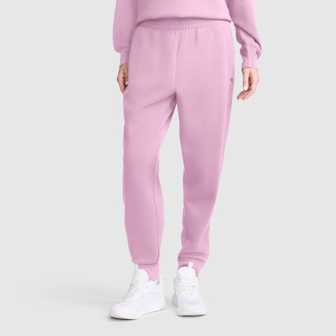 A person wearing the Champion Taper Leg Jogger with Zippers in light pink, paired with a matching pink sweatshirt and white sneakers, stands against a plain light gray background.