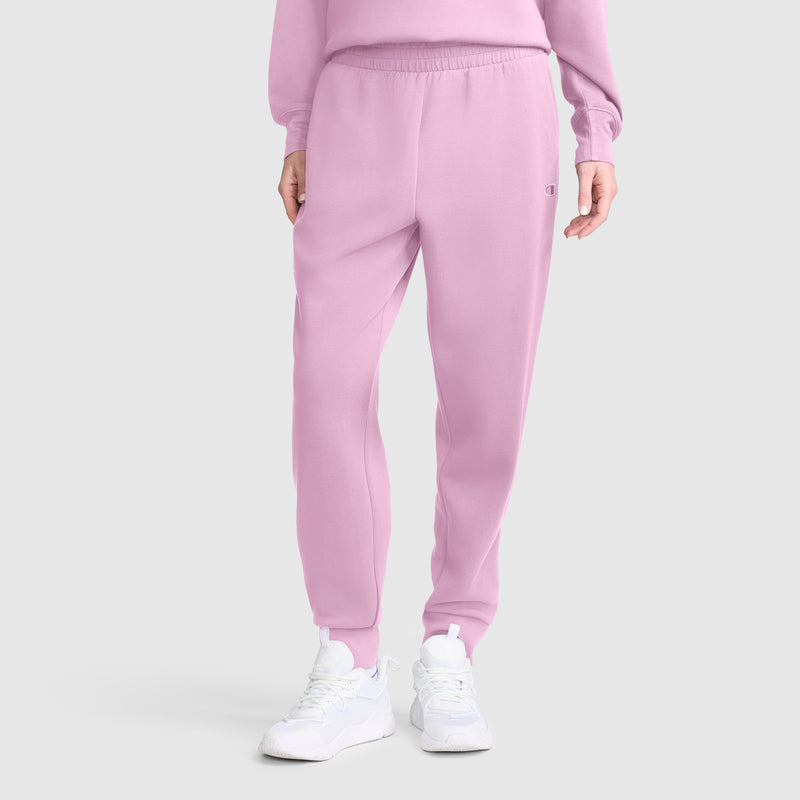 A person wearing the Champion Taper Leg Jogger with Zippers in light pink, paired with a matching pink sweatshirt and white sneakers, stands against a plain light gray background.