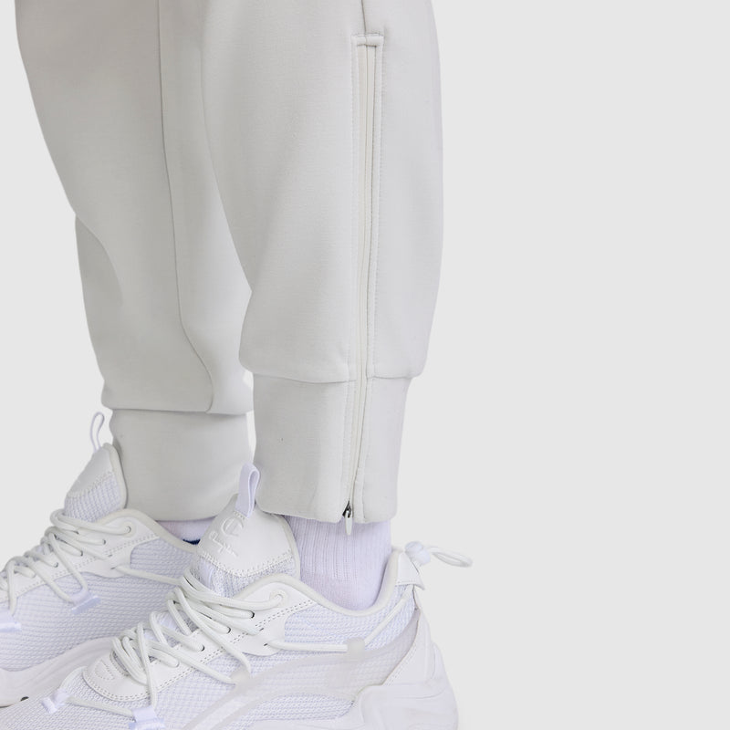 Close-up of a person wearing white sneakers, white socks, and the Champion Taper Leg Jogger with Zippers, featuring a tapered leg and side ankle zippers, standing on a plain light background.