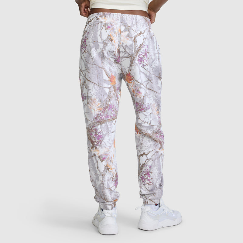 A person wearing white sneakers and Champion’s Powerblend Boyfriend Sweatpant with an allover gray, purple, and orange tree-branch print stands against a plain light background, facing away. The joggers feature a cinch bottom design that gives a modern update to classic Champion C Logo women’s sweatpants.