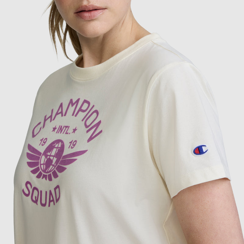 A woman wearing the Champion Squad Graphic T-Shirt, a cream-colored tee with a purple collegiate graphic design and a subtle Champion patch on the sleeve, crafted from lightweight cotton jersey for all-day comfort.
