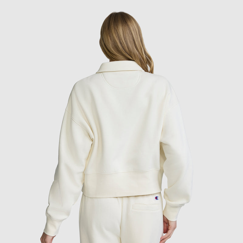 A person with long, light brown hair is seen from the back against a plain light background, wearing the Champion Fleece Training Polo and matching pants.