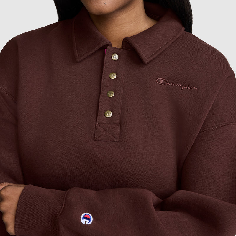 A person is seen wearing a Champion Fleece Training Polo in maroon, featuring a collared neckline and five-button placket. The stylish women’s fleece pullover has the Champion logo embroidered on both the left chest and sleeve. Only the lower face and upper body are visible.
