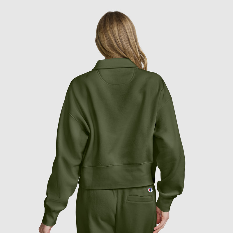 A person with long, light brown hair is shown from the back, wearing a matching olive green sweatshirt and sweatpants set against a plain white background, styled with the cozy comfort of the Champion Fleece Training Polo.