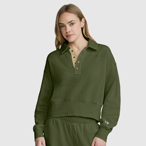 A woman with long blonde hair wears the Champion Fleece Training Polo in olive green, featuring a collar and matching pants, as she stands against a plain light gray background.
