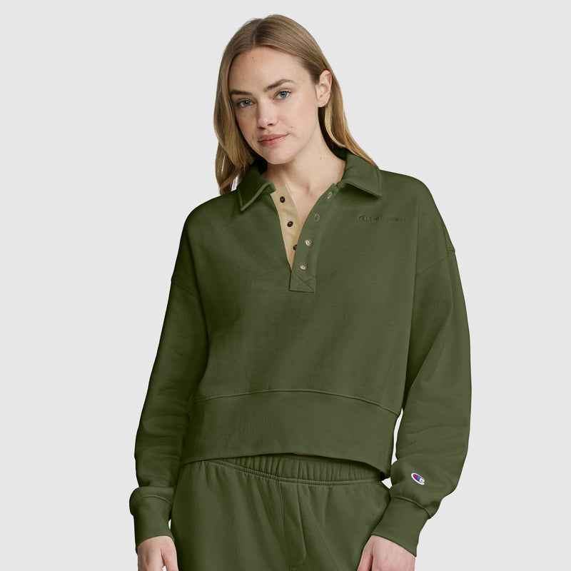 A woman with long blonde hair wears the Champion Fleece Training Polo in olive green, featuring a collar and matching pants, as she stands against a plain light gray background.