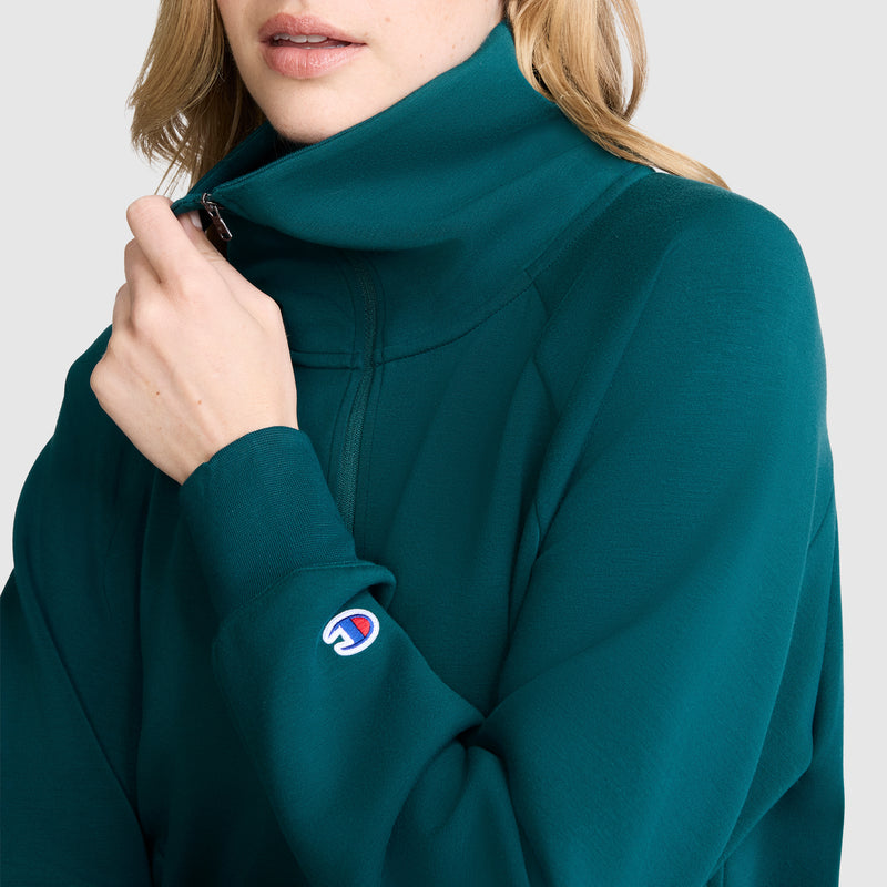 A person wearing a teal Champion Quarter-Zip Pullover with a high collar, partially zipped up. The athletic pullover has a small Champion logo patch near the wrist.