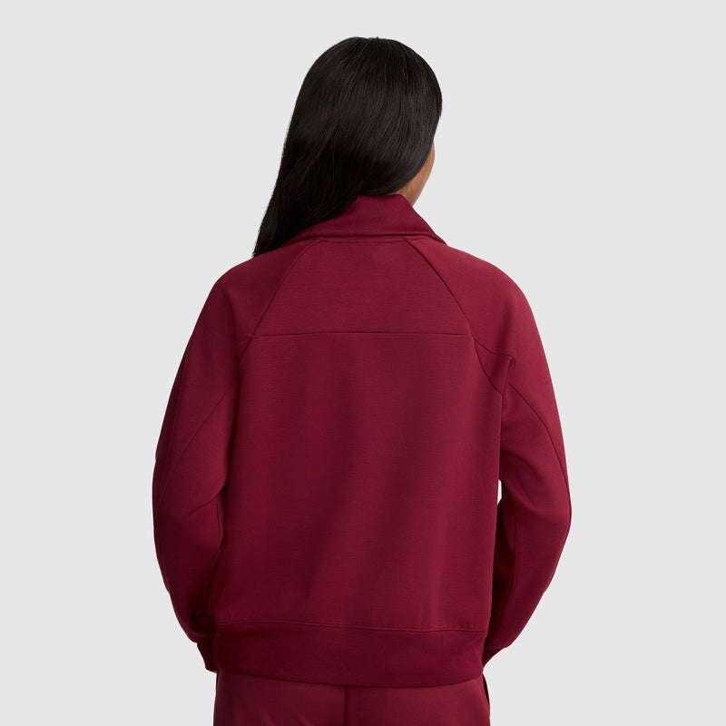 A person with long dark hair is shown from the back, wearing a maroon Champion Quarter-Zip Pullover made of stretch scuba blend fabric and matching pants, standing against a plain light gray background.