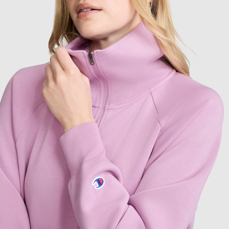 A woman wears the Champion Quarter-Zip Pullover in light purple, styled partially unzipped, with the brand’s small logo patch visible on the sleeve.