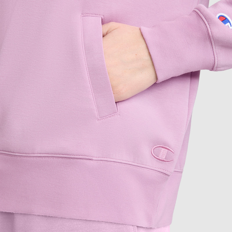 A person wearing a light purple Champion Quarter-Zip Pullover with one hand in the front pocket. The fabric features a small embroidered Champion logo near the wrist and another near the hem, showcasing the sporty design of this women's athletic Quarter-Zip Pullover.