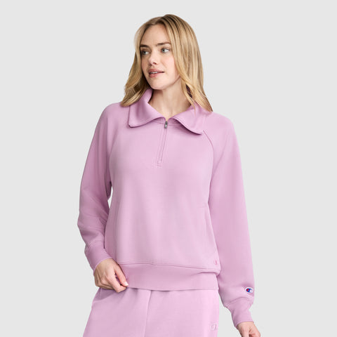A woman models the Champion Quarter-Zip Pullover in light purple with matching pants, featuring a zip-collar design, while standing against a plain light gray background and gazing slightly to the side.
