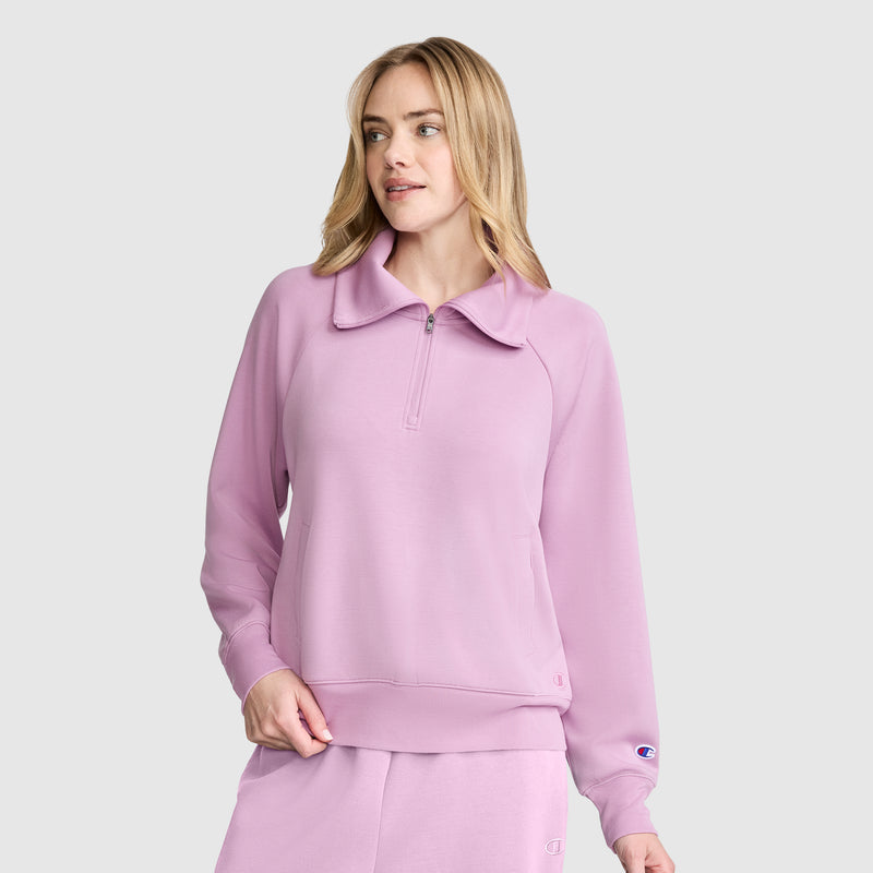 A woman models the Champion Quarter-Zip Pullover in light purple with matching pants, featuring a zip-collar design, while standing against a plain light gray background and gazing slightly to the side.