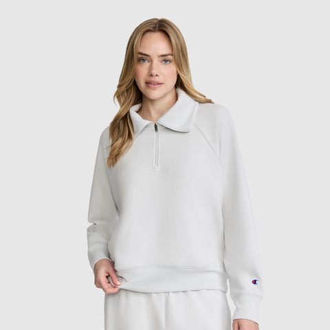 A woman stands against a plain light background, looking at the camera with a relaxed expression. She’s wearing a light gray Champion Quarter-Zip Pullover and matching stretch poly-modal pants.
