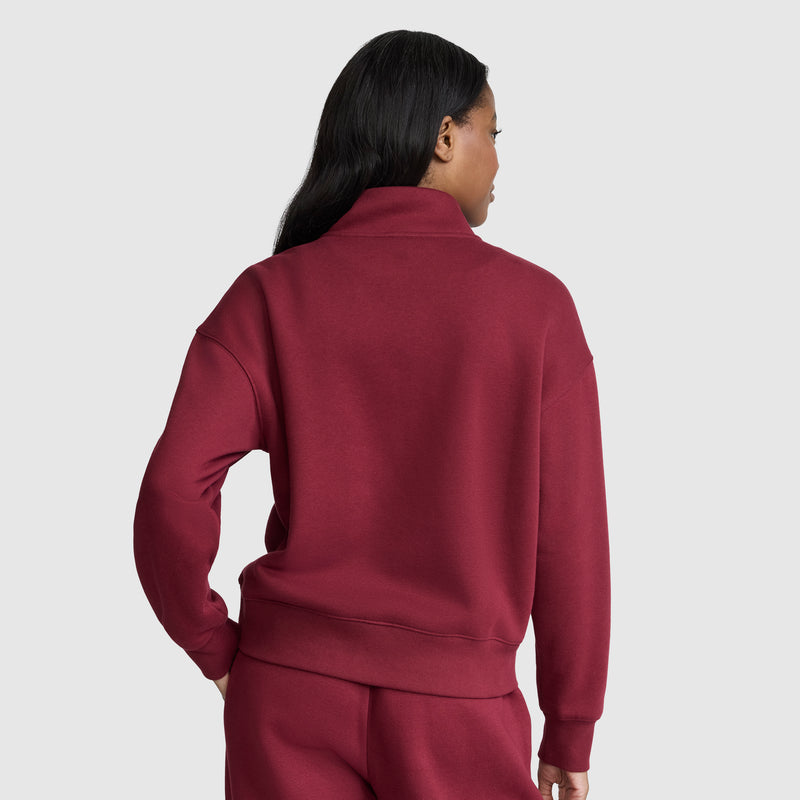 A person with long dark hair stands with their back to the camera against a plain light gray background, wearing a matching maroon Champion Fleece Mockneck Quarter-Zip and sweatpants, embodying a relaxed sport style.