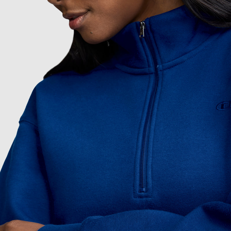 A person is shown from the shoulders up wearing a royal blue Champion Fleece Mockneck Quarter-Zip. The zipper is pulled halfway, and the image highlights the soft fabric and upper chest area, emphasizing its sporty style.