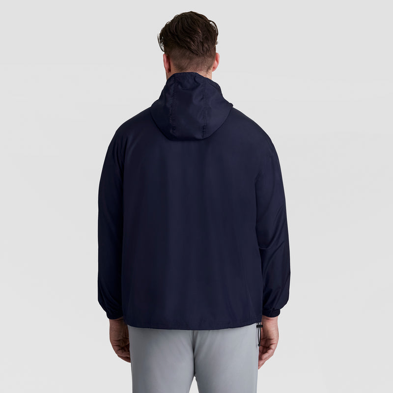 A man is seen from behind wearing the Champion Stadium Packable Jacket, Script Logo - Big & Tall in navy blue with light gray pants, posed against a plain, light background.