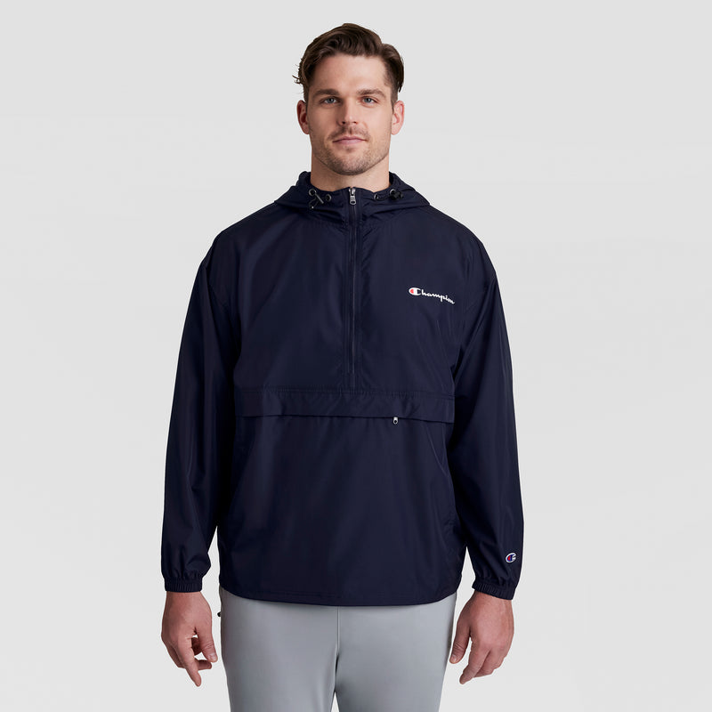 A man faces forward wearing a navy blue Champion Stadium Packable Jacket, Script Logo - Big & Tall, with light gray pants against a plain light gray background.
