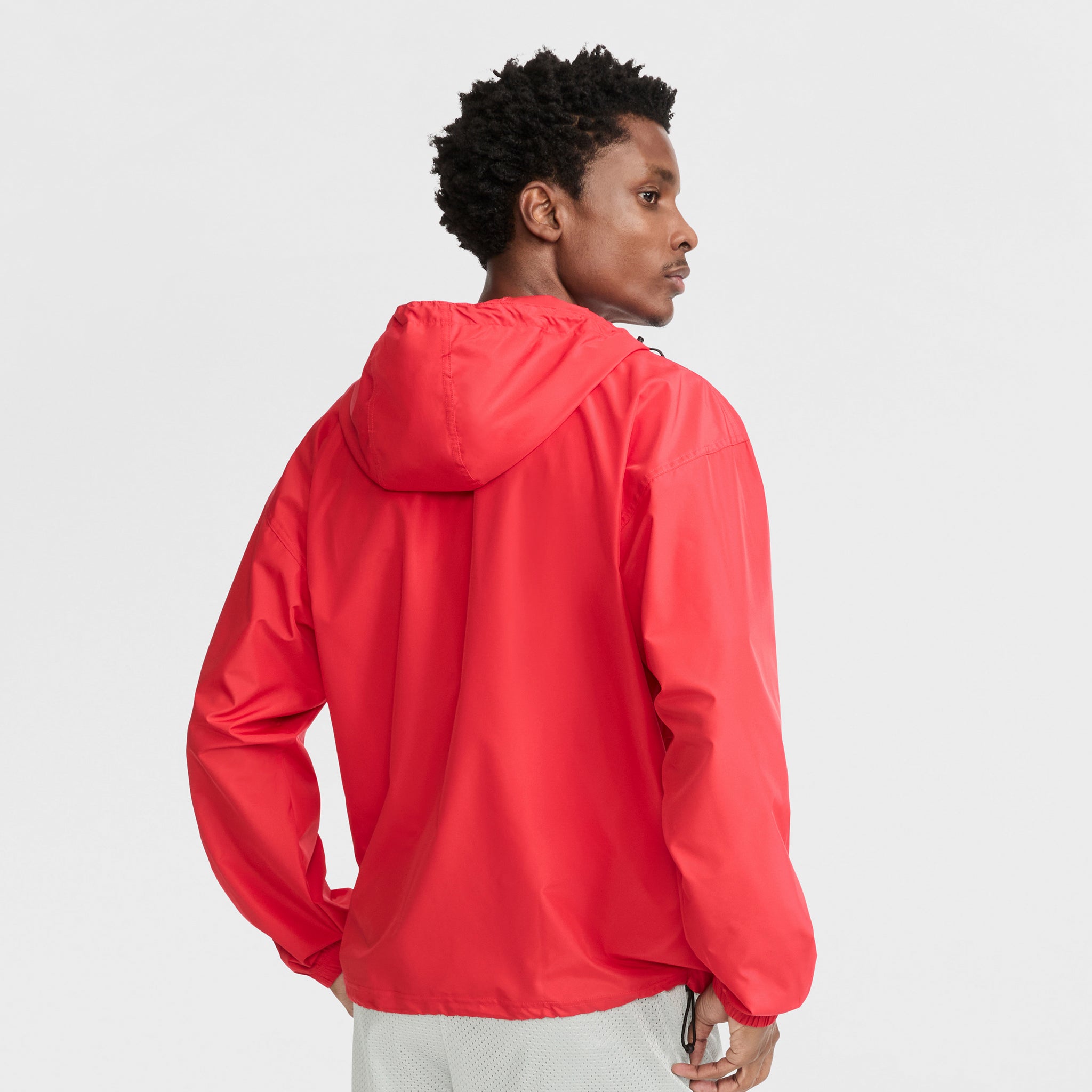 A person in a bright red Champion Stadium Packable Jacket with Script Logo stands turned slightly to the side, looking over their shoulder against a plain white background.