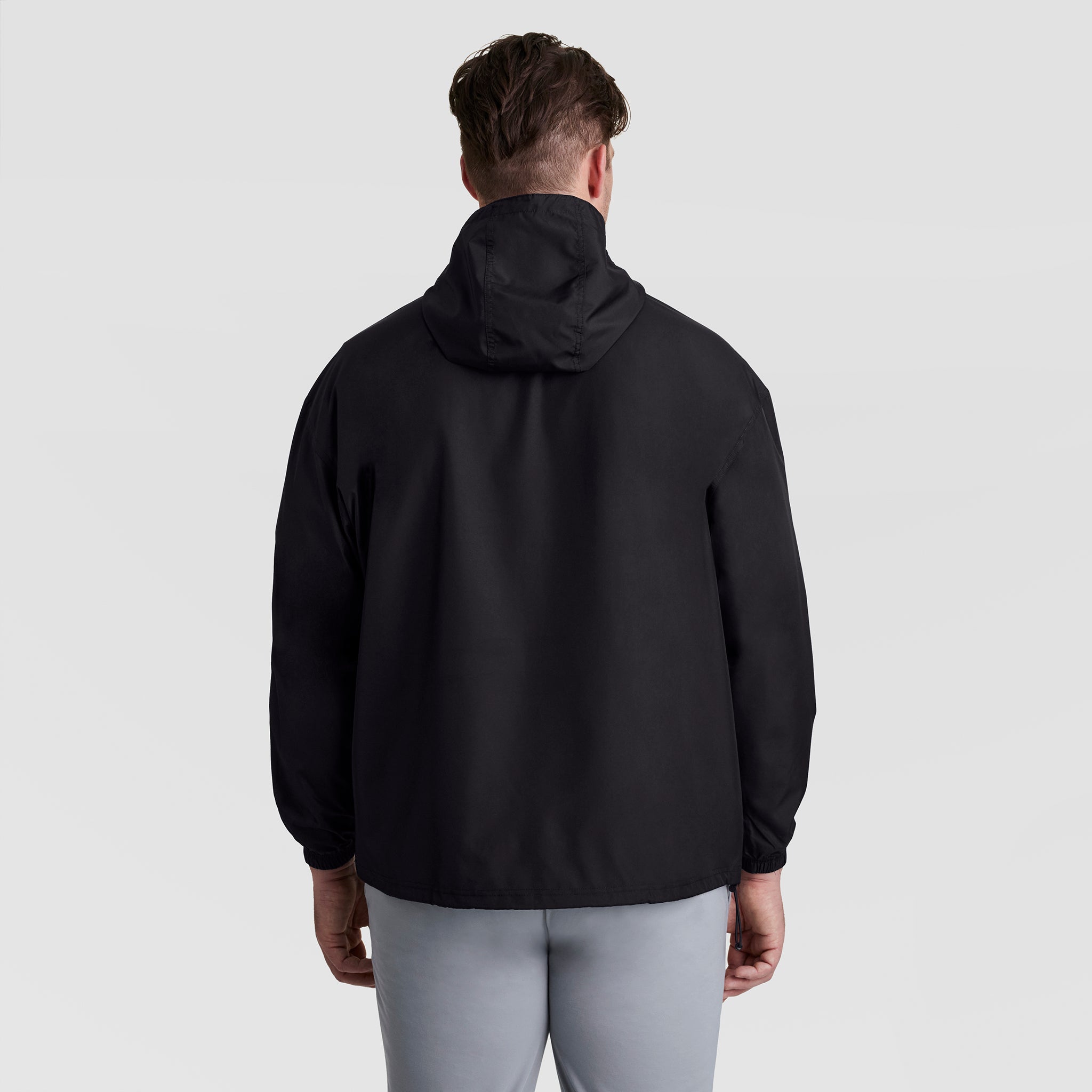 A person faces away from the camera wearing the Champion Stadium Packable Jacket, Script Logo - Big & Tall in black and light gray pants, standing against a plain light gray background.