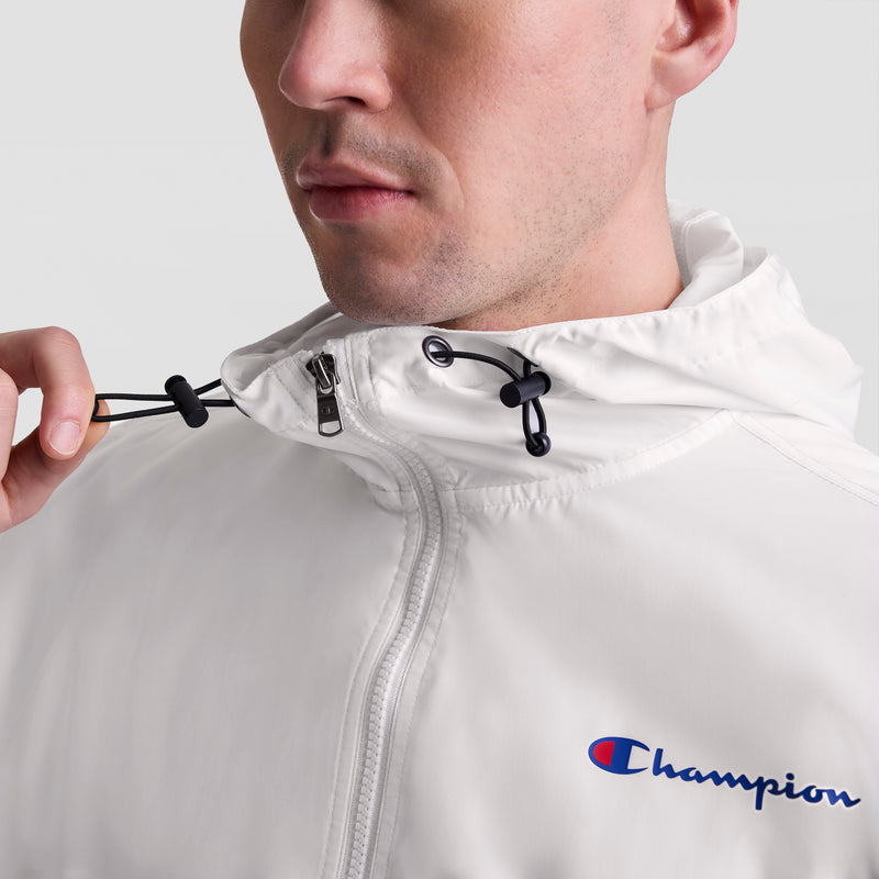 Close-up of a man wearing the Champion Stadium Packable Jacket, Script Logo, in white, adjusting the hood’s drawstring.