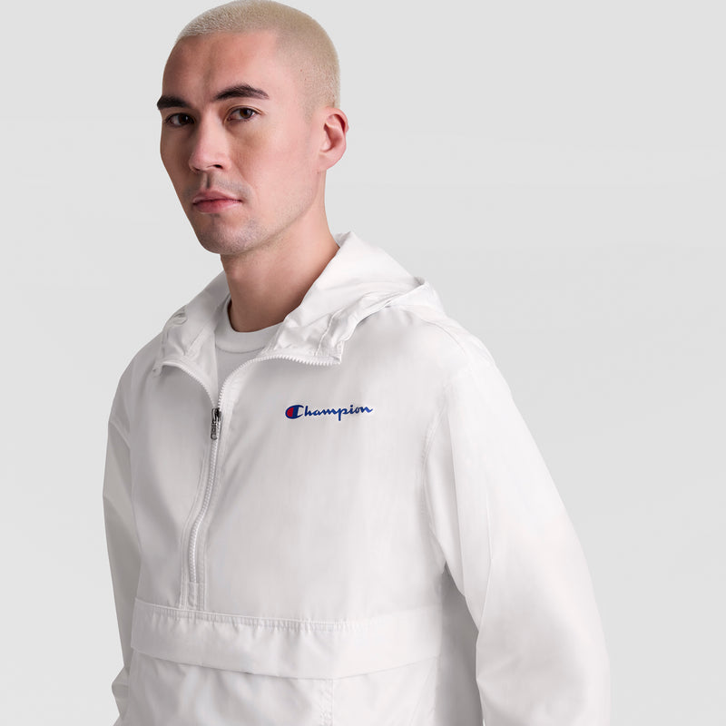 A person with short blond hair wears a white Champion Stadium Packable Jacket with script logo and front zipper, standing against a plain light gray background.