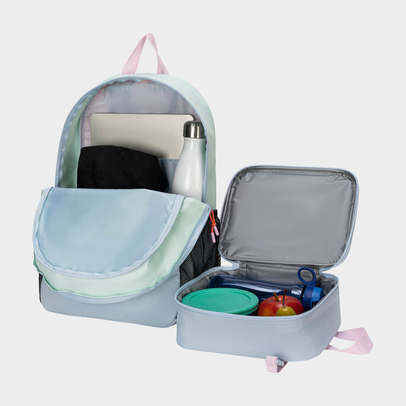 The Champion Kids' Mode Lunch Kit & Backpack Combo is displayed on a white background. The pastel backpack is open with a water bottle, folder, and black item inside; the open insulated lunch kit holds an apple, container, and blue item.
