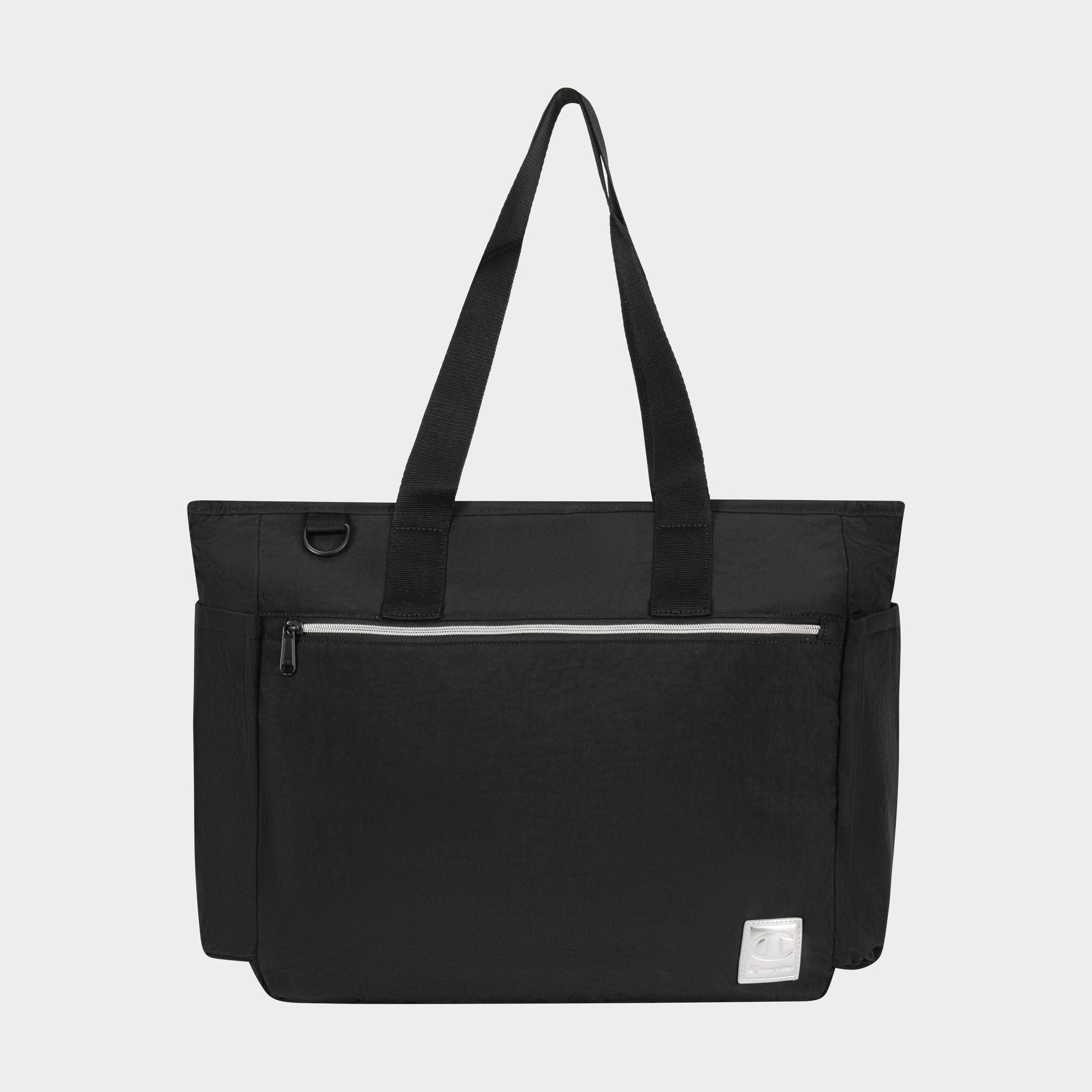 The Champion Quartz East West Tote is a black lightweight crinkle nylon bag featuring two shoulder straps, a front zip pocket, side pockets, a padded laptop sleeve, and a white logo patch on the bottom right, shown on a plain light background.