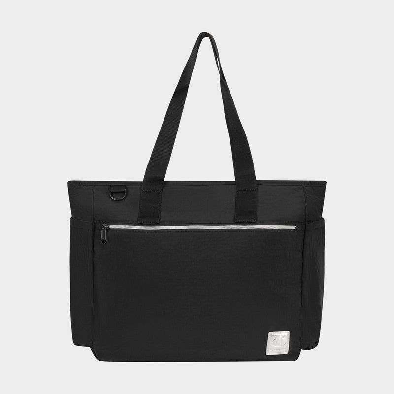 The Champion Quartz East West Tote is a black lightweight crinkle nylon bag featuring two shoulder straps, a front zip pocket, side pockets, a padded laptop sleeve, and a white logo patch on the bottom right, shown on a plain light background.
