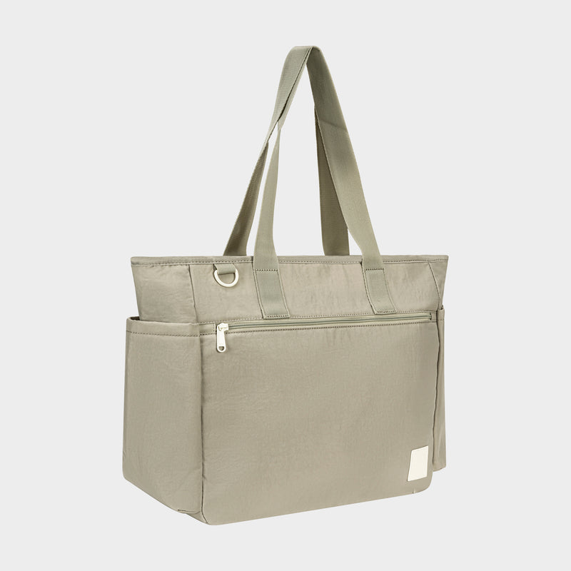 The Champion Quartz East West Tote in light olive green features two long handles, a front zippered pocket, side pockets, padded laptop sleeve, and a small white patch near the bottom corner, shown on a plain white background.