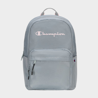 The Champion Steady Backpack in light gray features a front zip pocket, black zipper pulls, small Champion logo patch, large white Champion script on top, and a top handle. Roomy enough for essentials like your laptop.