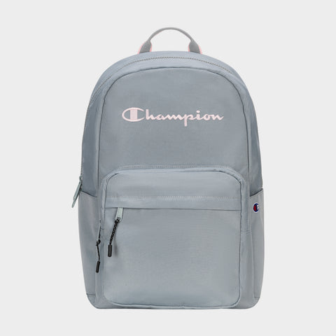 The Champion Steady Backpack in light gray features a front zip pocket, black zipper pulls, small Champion logo patch, large white Champion script on top, and a top handle. Roomy enough for essentials like your laptop.