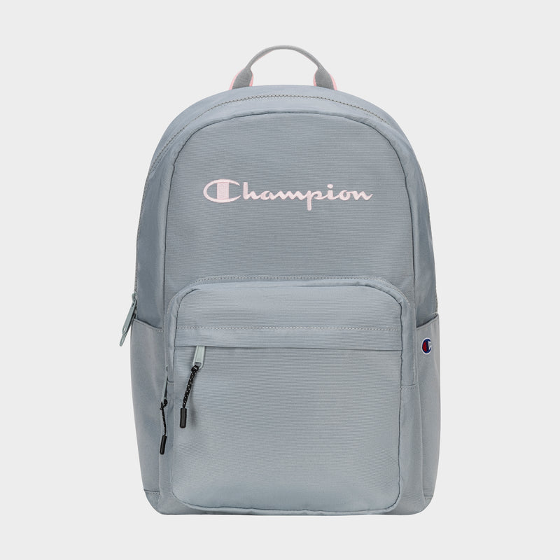 The Champion Steady Backpack in light gray features a front zip pocket, black zipper pulls, small Champion logo patch, large white Champion script on top, and a top handle. Roomy enough for essentials like your laptop.
