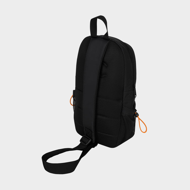 The Champion Camden Sling backpack in black features a single adjustable strap and is made from durable nylon sling material. It includes a mesh back panel, two small side pockets accented with orange zipper pulls, and a top carrying handle. The bag is displayed against a plain light gray background.