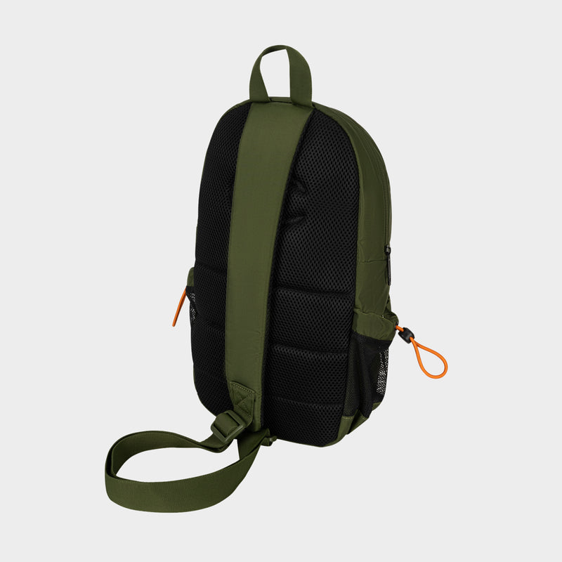 A Champion Camden Sling backpack in green and black is displayed from the back, highlighting padded straps, a single adjustable strap, and distinctive orange zipper pulls. Made from durable nylon, this sling bag is set against a light gray background.
