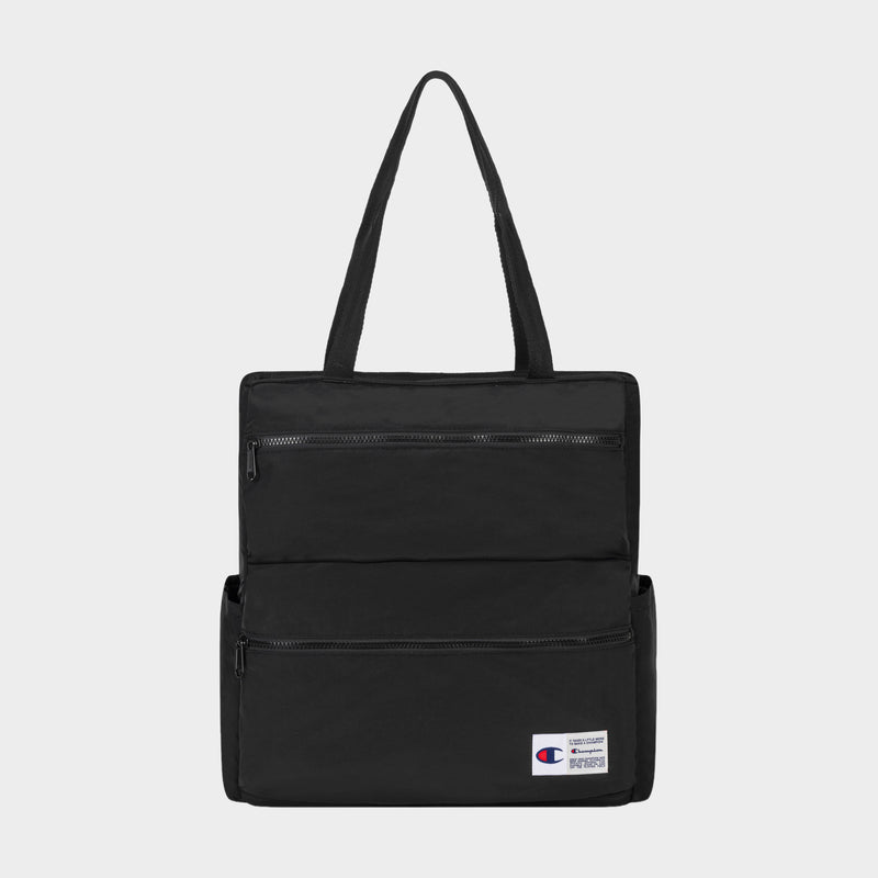 The Champion Explore Tote is crafted from durable crinkle nylon in black and features two zippered front pockets, convenient side pockets, and a small Champion logo patch on the lower right corner. Inside, a padded laptop sleeve adds functionality. The product is displayed against a plain white background.