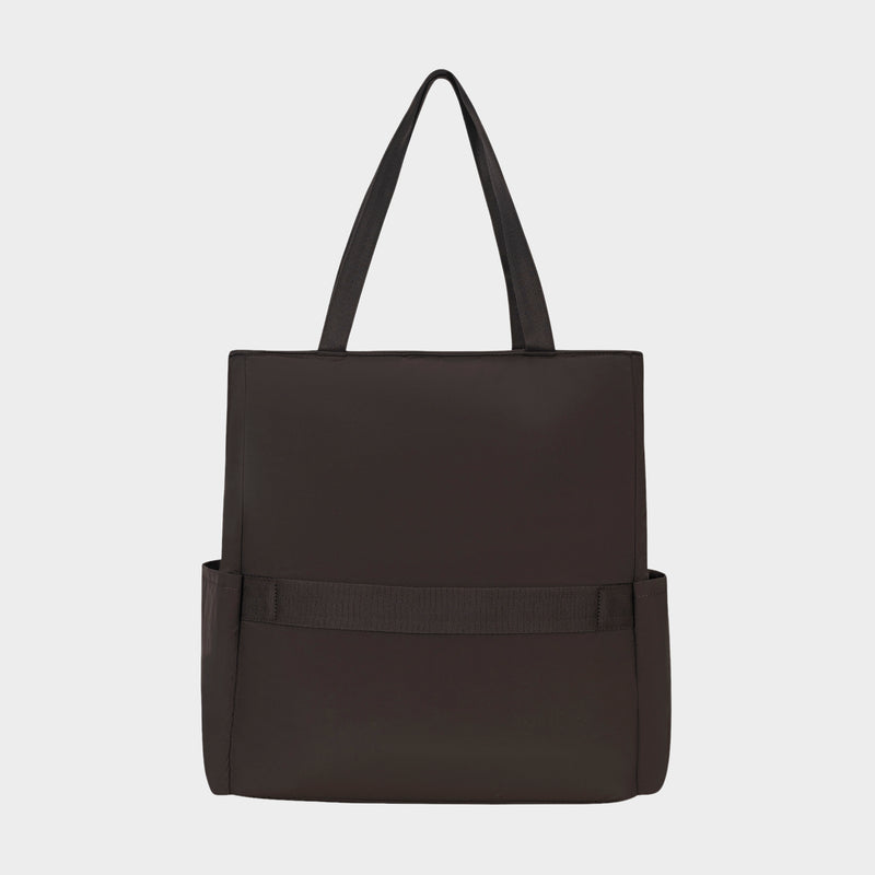 The Champion Explore Tote, shown against a plain white background, is a black rectangular tote bag made from durable crinkle nylon with two handles, side pockets, and a horizontal strap on the front. It also features a padded laptop sleeve.