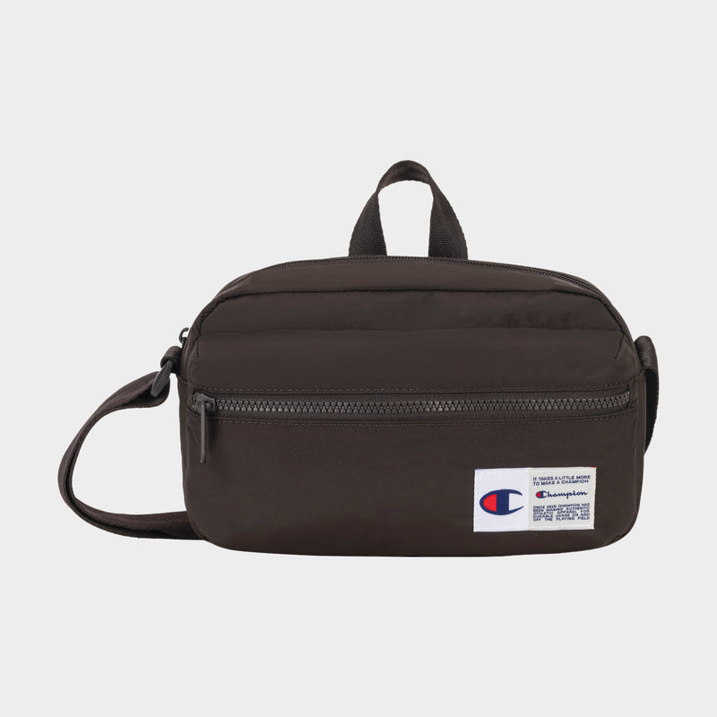 The Champion Explore Crossbody is a small black bag crafted from durable crinkle nylon, featuring a front zipper pocket, top handle, and adjustable strap. A Champion logo patch accents the lower right corner. The product is displayed against a plain white background.