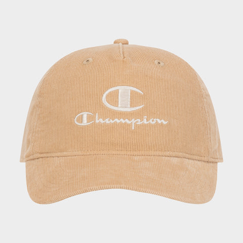 Introducing the Pursuit Corduroy Adjustable Cap by Champion—a tan corduroy baseball cap featuring the word “Champion” and a bold C logo embroidered in white on the front. Designed with a curved brim and an adjustable snapback closure, this cap offers timeless style and personalized comfort. It is showcased against a plain background.
