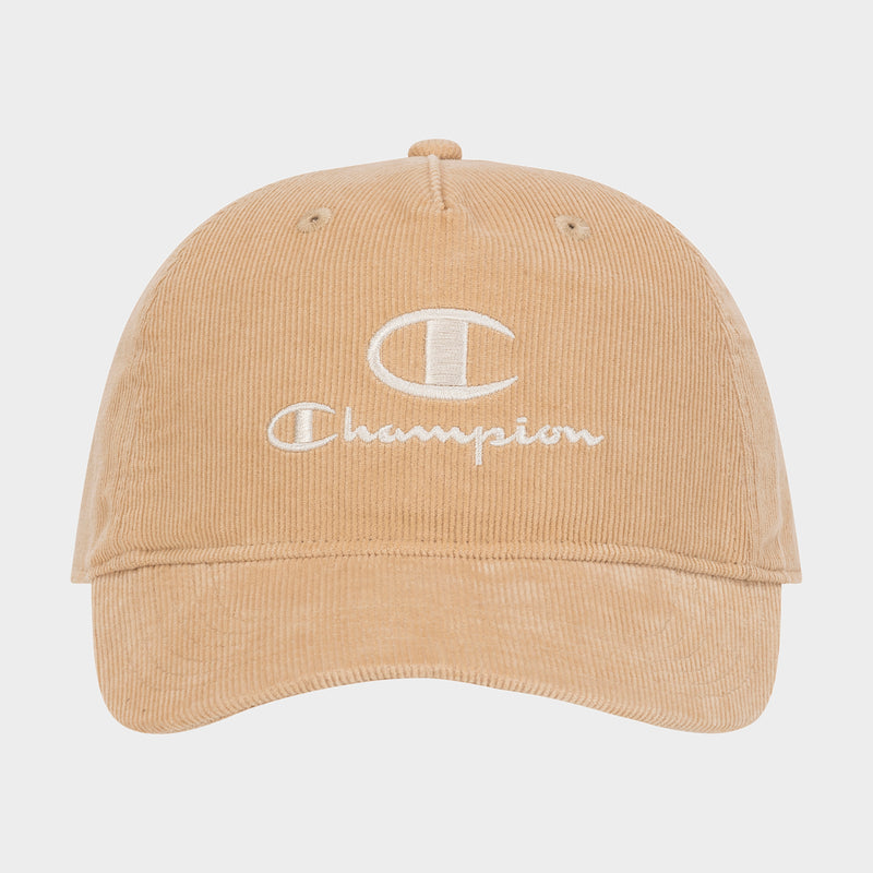 Introducing the Pursuit Corduroy Adjustable Cap by Champion—a tan corduroy baseball cap featuring the word “Champion” and a bold C logo embroidered in white on the front. Designed with a curved brim and an adjustable snapback closure, this cap offers timeless style and personalized comfort. It is showcased against a plain background.