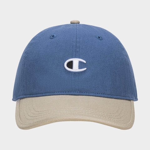 The Champion Briggs Washed Cotton Twill Adjustable Baseball Cap in blue features a beige brim and an embroidered white C logo on the front, displayed against a plain white background.