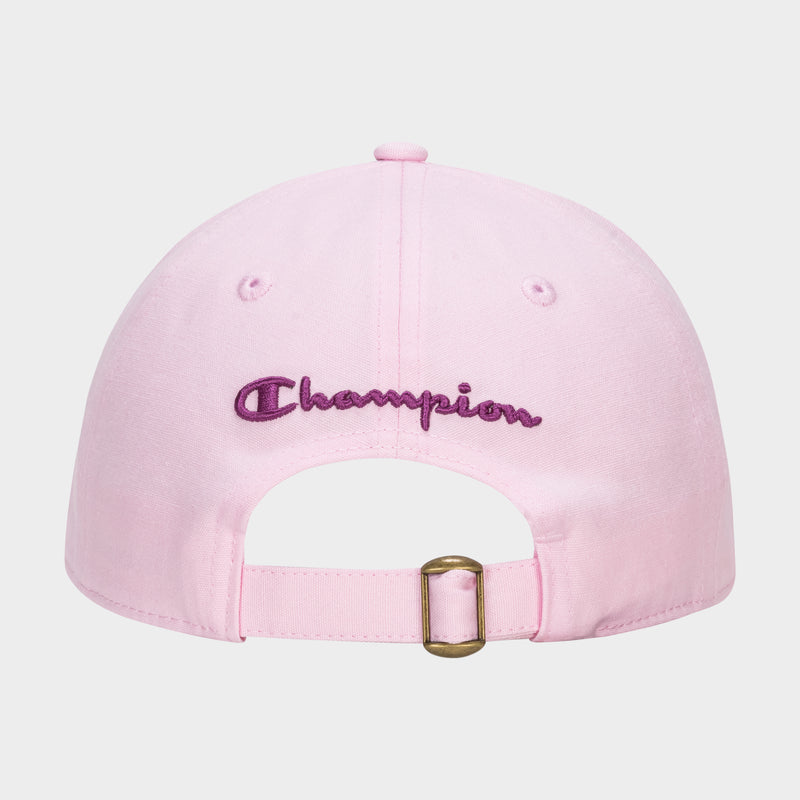 The Amber Chenille Adjustable Baseball Cap by Champion is shown from the back in light pink slub canvas, with "Champion" embroidered in purple above an adjustable strap featuring a brass buckle. The background is plain white.