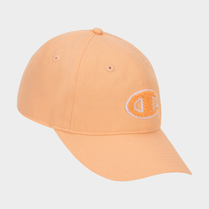 The Amber Chenille Adjustable Cap by Champion features a peach-colored, relaxed fit with a curved brim and an embroidered chenille “C” patch on the front left panel, displayed against a plain white background.