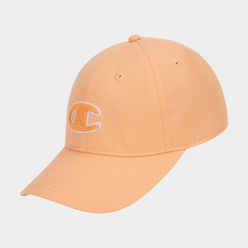 The Amber Chenille Adjustable Cap by Champion is peach-colored with a relaxed fit, featuring a curved brim and a white and yellow chenille C logo patch embroidered on the front. The cap is displayed against a plain white background.