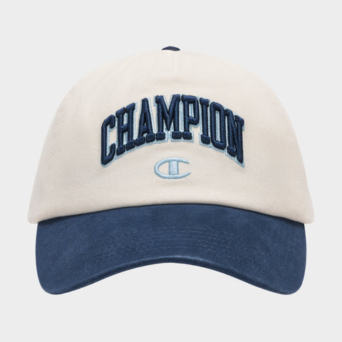 The Champion Amor Adjustable Baseball Cap features beige cotton twill, a dark blue brim, "CHAMPION" embroidered in blue on the front, and a light blue Champion logo.