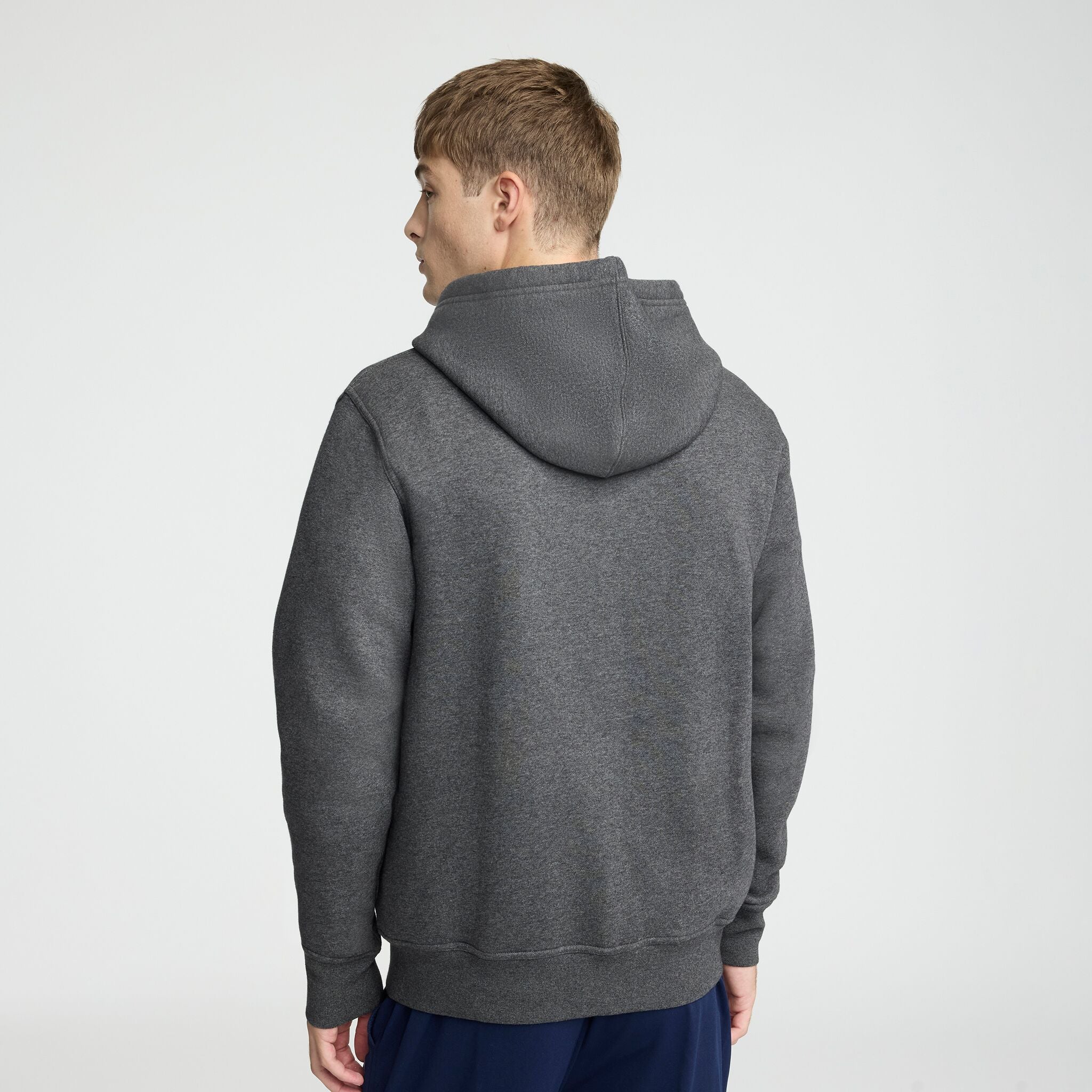 A person with short light brown hair is seen from the back, wearing a dark gray Champion Powerblend Full-Zip Hoodie, C Logo, and dark blue pants against a plain light background.